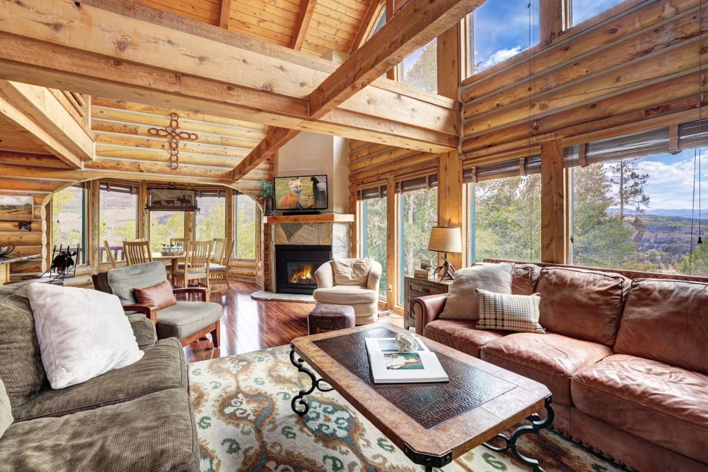 Great room with exposed log walls, vaulted timber ceiling, leather seating, and a stone fireplace